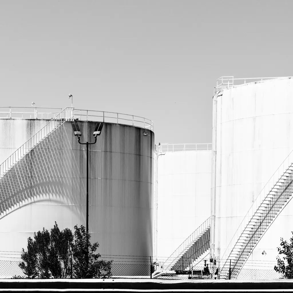 Black and white view of large steel storage tanks with spiral stairs